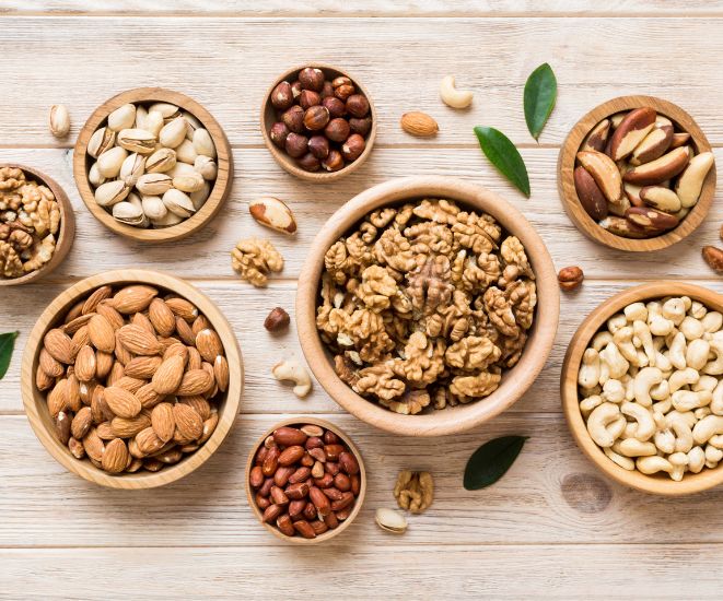 Various bowls holding different kinds of nuts, include almonds, walnuts, peanuts, hazelnuts and more.