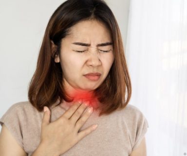 A woman with her eyes closed, holding a hand to her neck. There is a red highlight there to show throat pain.