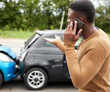 A man standing in front of a fender-bender car accident, talking on his phone.